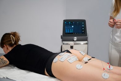 Patient receiving Z Stim electrode-based muscle stimulation on the buttocks and thighs, with the treatment system and practitioner visible.